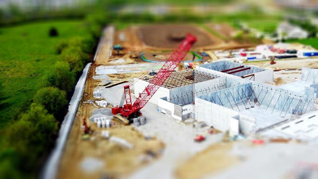 pexels-photo-392031-392031 Aerial view of a construction site with a red crane amidst green fields and concrete buildings.
